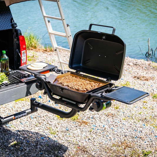 Cast iron flat top griddle on outdoor grill, open lid revealing hinged cooking surface