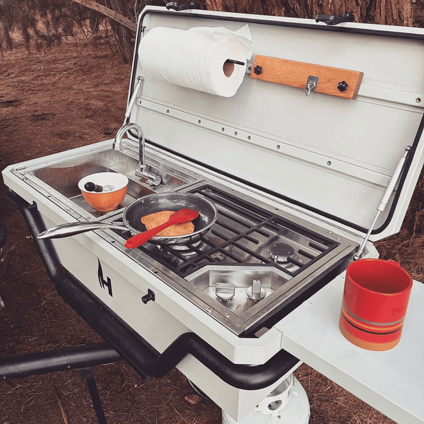 Open outdoor kitchen cooktop with grill grates, pot, and orange serving bowl