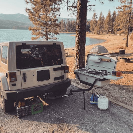 Vehicle-mounted outdoor kitchen with open grill, sink, and fuel container