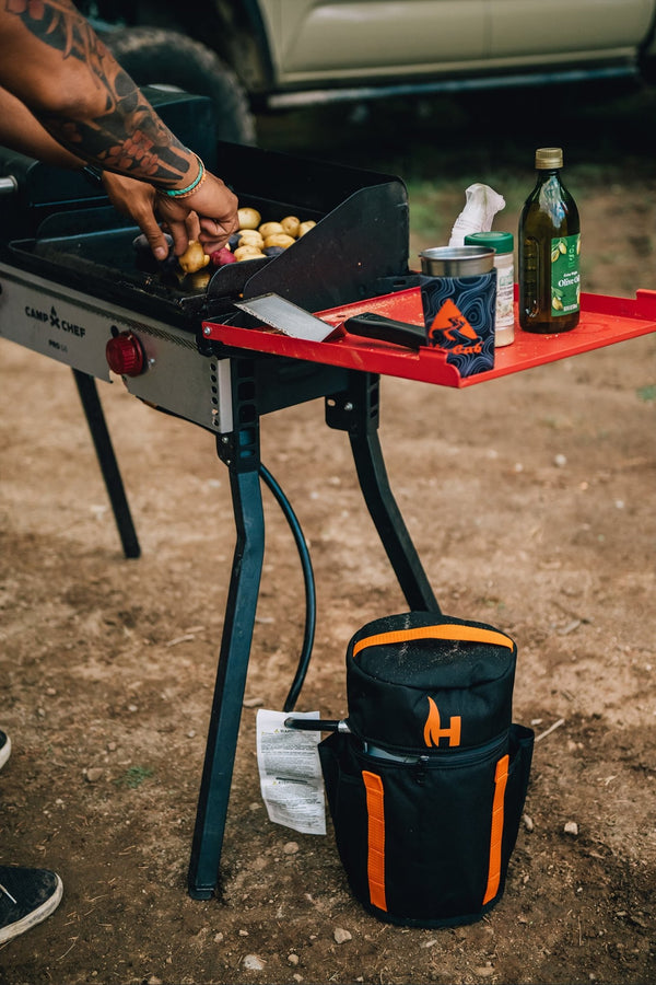 Refillable propane tank with black carrying case, connected hose near a grill