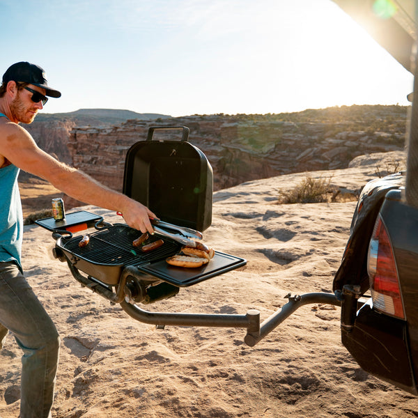 Hitch mounted propane grill with open lid and cooking grate, dark body with front controls.