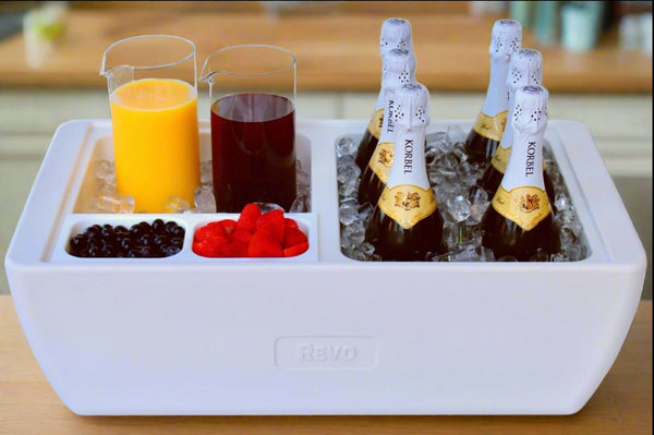 White party cooler bin with ice, cups of drink, fruit, and champagne bottles