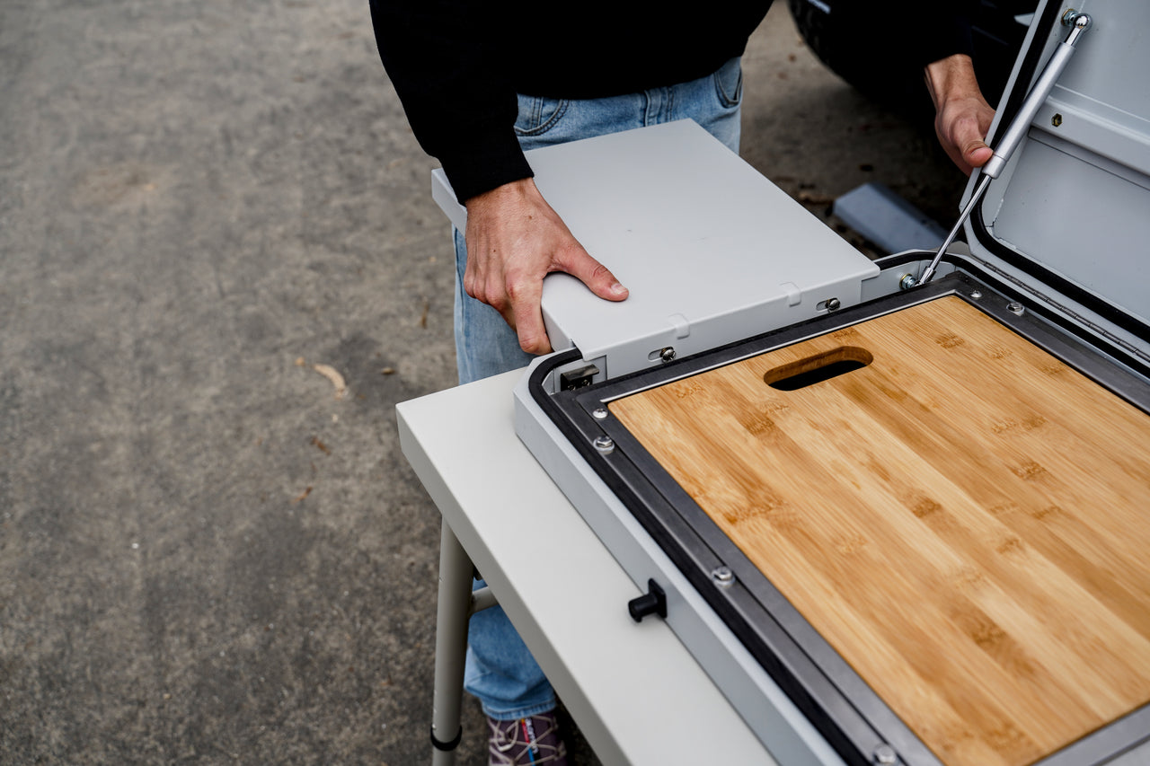 Camp kitchen unit with open lid and mounted wooden cutting board