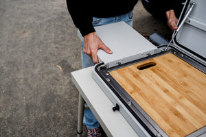 Camp kitchen unit with open lid and mounted wooden cutting board