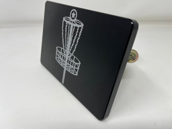 Disc golf hitch cover with metal chain-and-basket emblem on dark plate