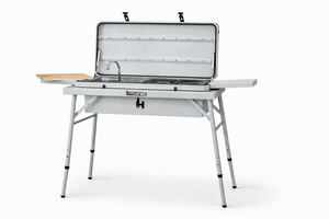 Camp kitchen grill with open lid, sink, grates, and side shelf