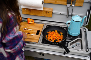 Camp kitchen grill interior with skillet of food and blue kettle on cooktop