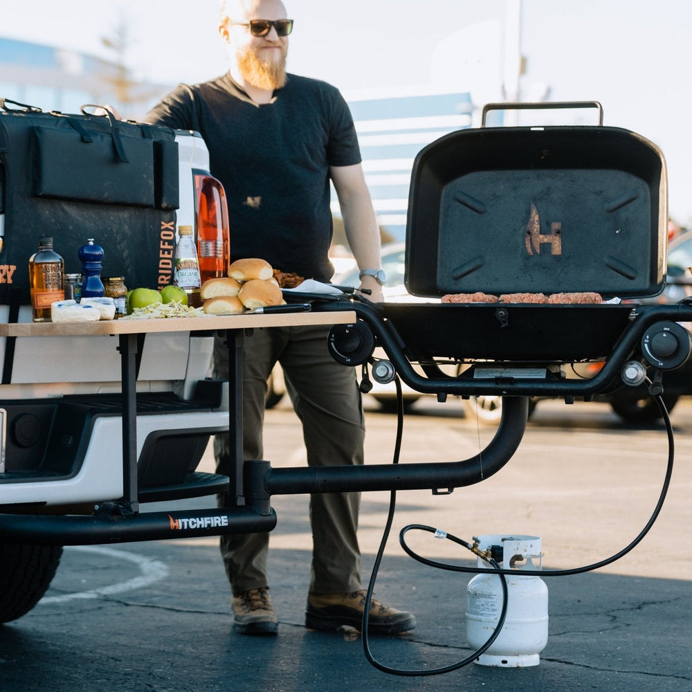 Hitch mounted propane grill with open lid and dual side shelves, dark finish with knobs.