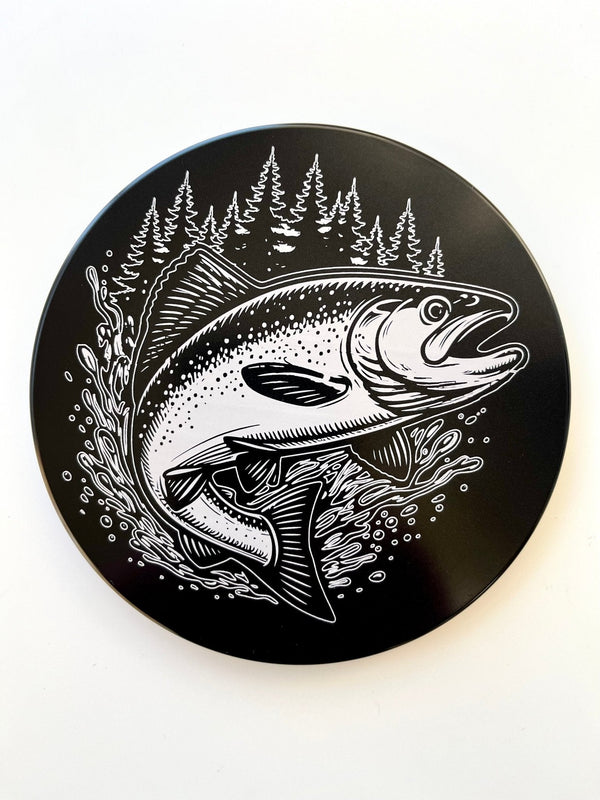 Round hitch cover with king salmon graphic and pine trees illustration on dark background