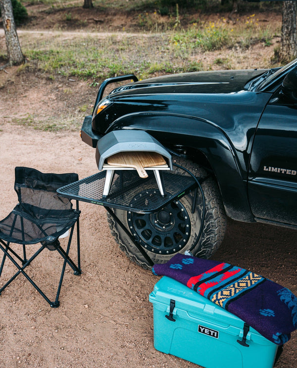 Large black aluminum camping table with wire mesh top and folding legs on outdoor ground
