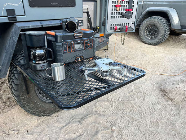Black steel camping table with wire-mesh top and folding legs
