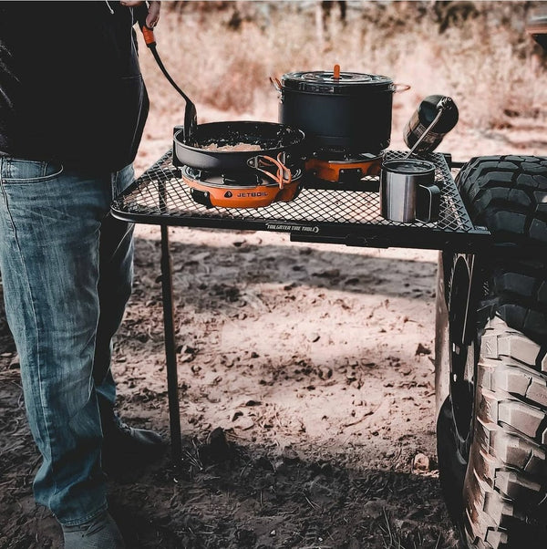 Black steel camping table with rectangular wire-mesh surface for cookware
