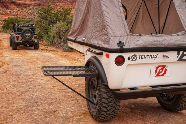 Black steel camping table with wire-mesh top extended from a trailer