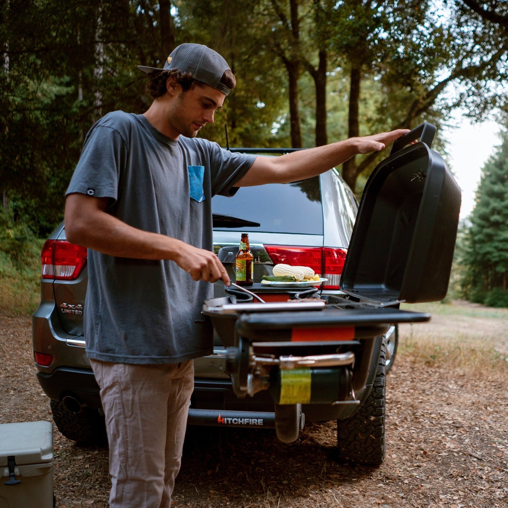 Hitch-mounted propane grill with open lid being used for grilling