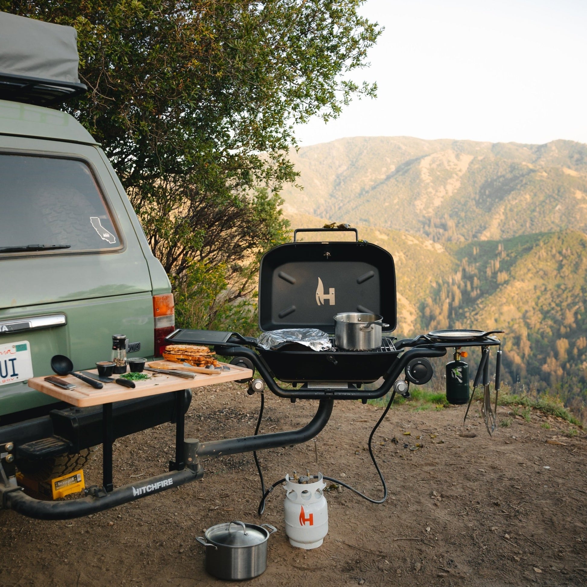 Hitch mounted propane grill with closed lid and connected propane tank, dark finish on hitch.