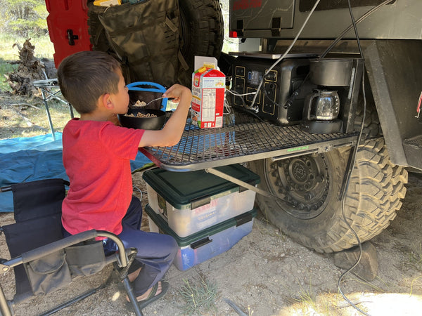 Black wire mesh camping table with a raised edge, used for cookware during camping.