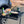 Load image into Gallery viewer, Black wire mesh camping table with raised edge, holding a skillet and bottles.
