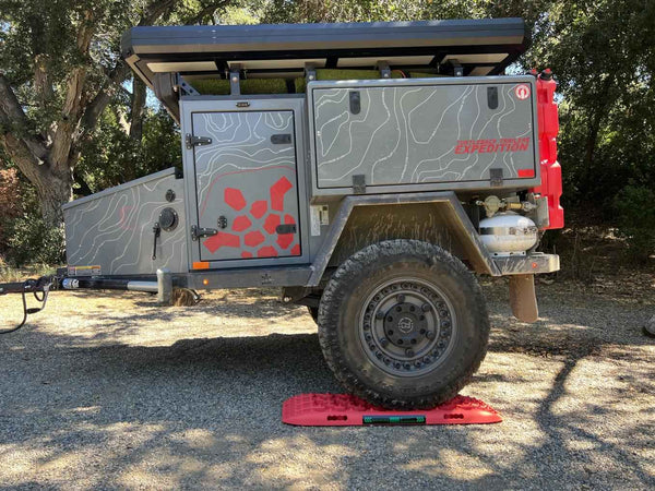 Red off-road tire recovery board with raised traction studs on asphalt