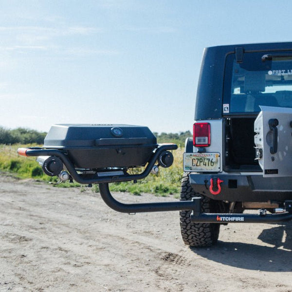 Hitch-mounted propane grill with black lid, front burner knobs, and rear support