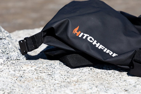 Black grill cover with HitchFire logo and strap buckle on stone surface