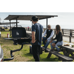 Black hitch-mounted propane grill with lid closed and two front side shelves