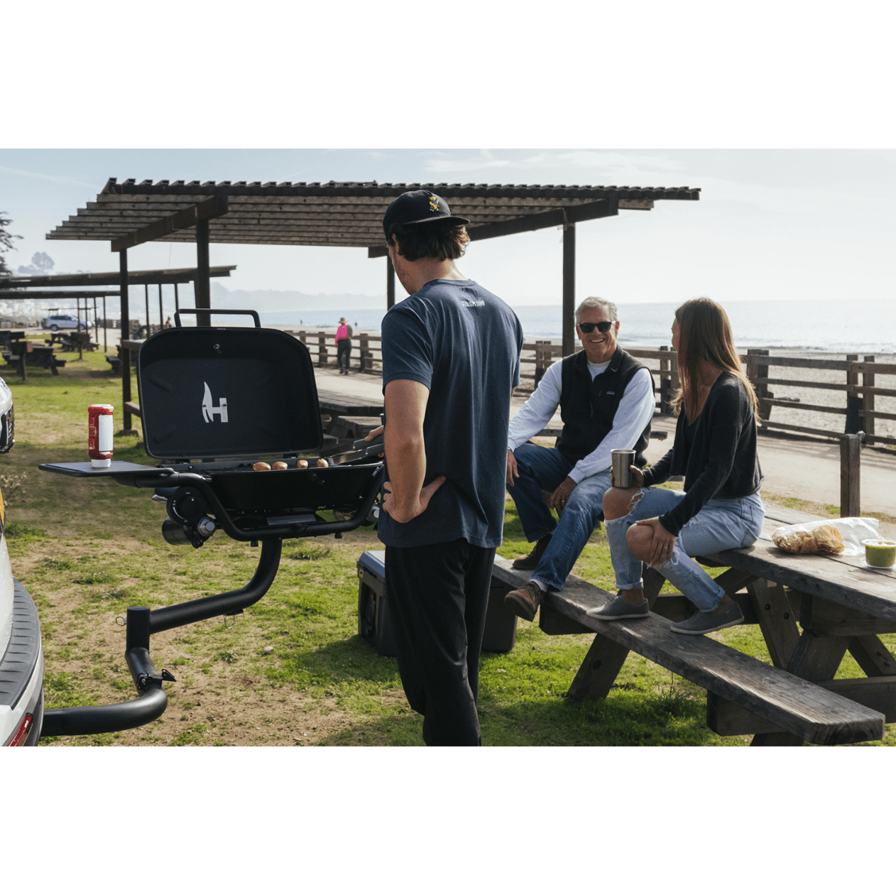 Black hitch-mounted propane grill with lid closed and two front side shelves