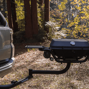 Black hitch-mounted propane grill with side shelves and round lid temperature gauge