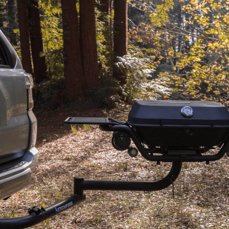 Black hitch-mounted propane grill with side shelves and round lid temperature gauge